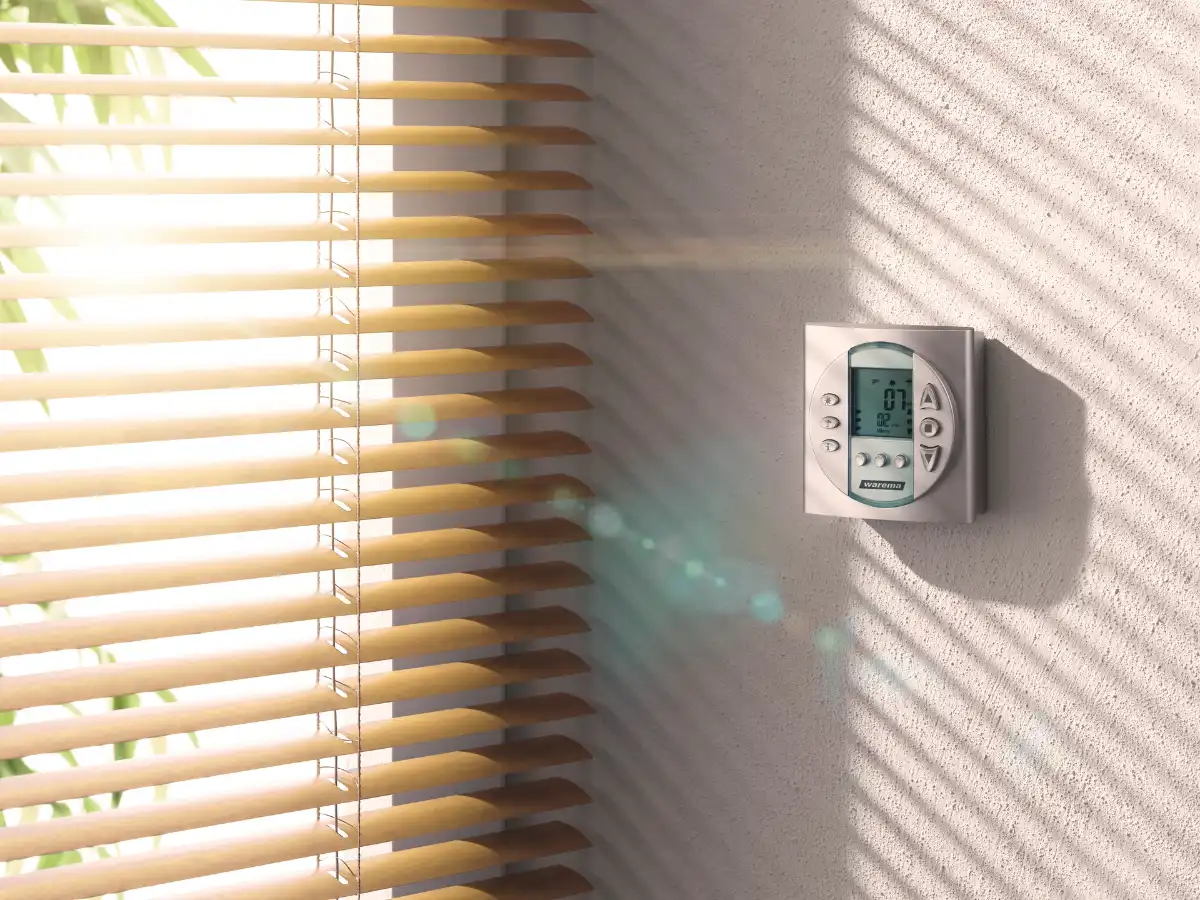 Digitales Thermostat an einer Wand neben Innenjalousien