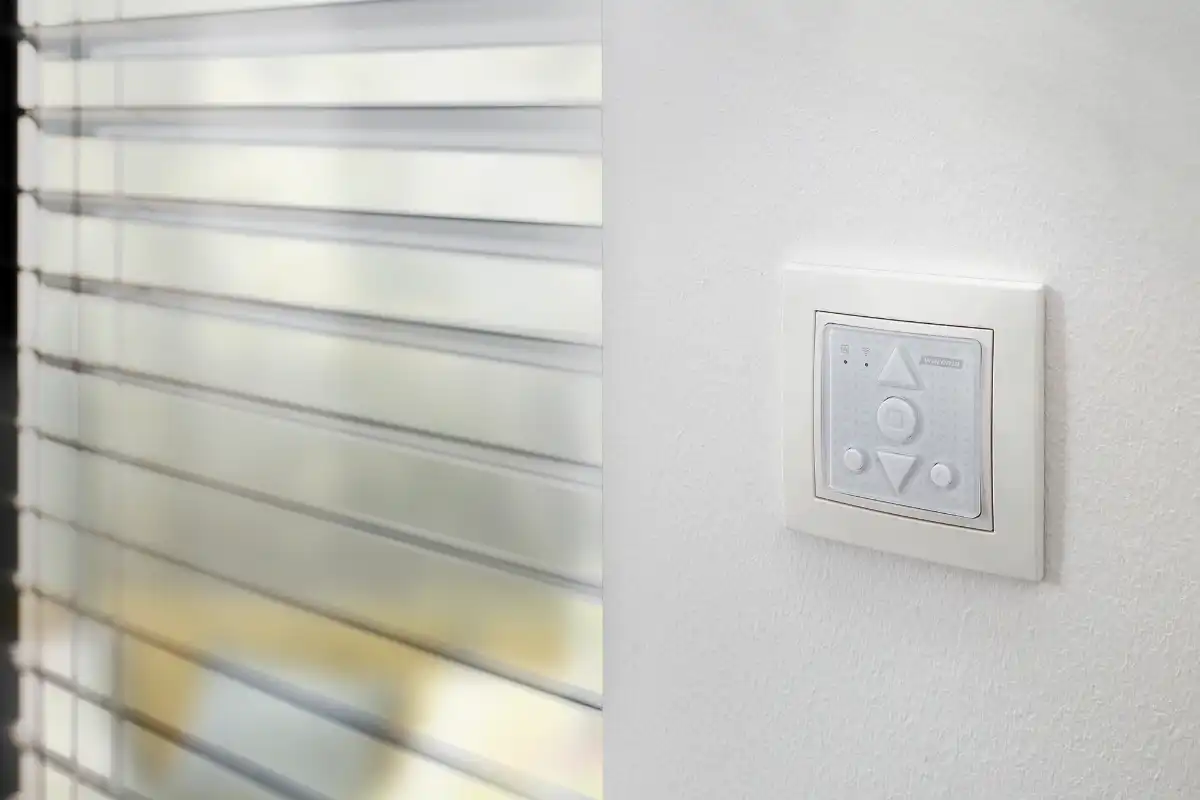 Elektrischer Rollladenschalter an der Wand neben geschlossenen Jalousien