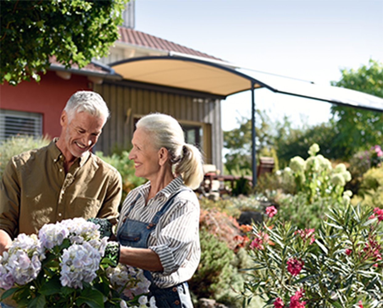 Ein älteres Ehepaar im Garten mit einer Schatten spendenen Markise im Hintergrund.