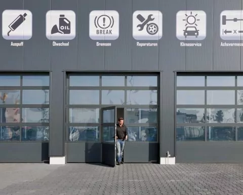 Ein Mann kommt aus der Tür in einem großen grauen Industrietor mit Sichtfenstern.